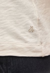 Tissu beige texturé avec de petites lettres marron M, O, P près de l'ourlet au-dessus d'un tissu en denim foncé.
