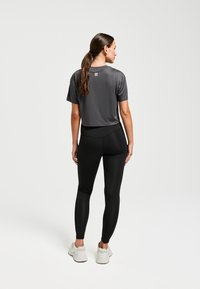 Grijze cropped T-shirt gemaakt van zacht materiaal, gecombineerd met zwarte leggings. De outfit heeft een eenvoudig ontwerp en een neutraal kleurenpalet.