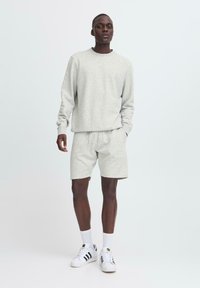 Sudadera gris y pantalones cortos de tela suave, con un corte relajado. Combinados con zapatillas blancas y calcetines de longitud media.