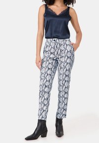 Marineblauw satijnen camisole met kantafwerking, gecombineerd met wit en marineblauw slangenprint tapered broek met zakken en aansluitende zwarte enkelboots.