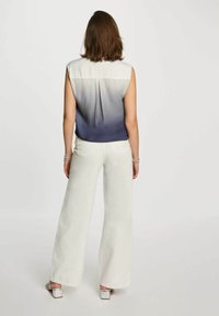 Blusa senza maniche con gradiente che passa dal bianco al blu navy, abbinata a pantaloni bianchi a palazzo e sandali argentati, vista da dietro.
