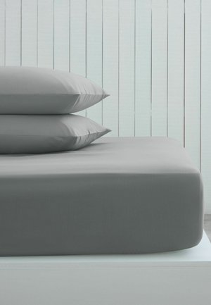 Two gray pillows stacked on a gray fitted sheet-covered mattress against a light wood paneled wall.