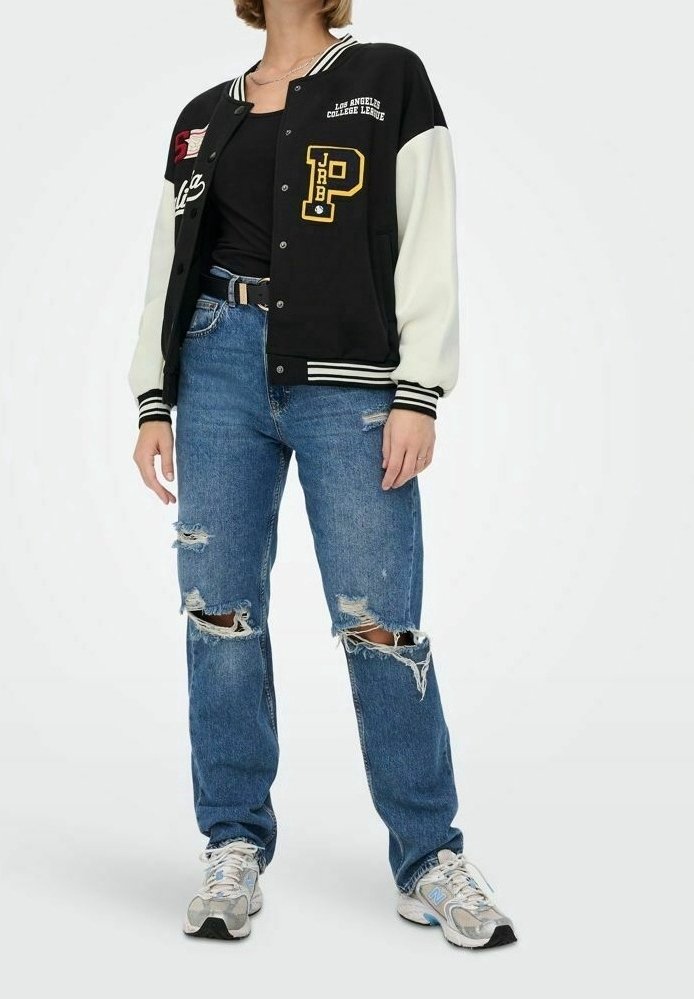 Czarna i biała kurtka varsity z naszywkami, noszona na czarnej bluzce, w połączeniu z zniszczonymi niebieskimi dżinsami i szarymi trampkami.
