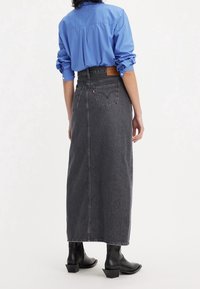 Černá džínsová sukně vysokého pasu se současným střihem, zadními kapsami a koženou nášivkou s logem. Kombinována s modrou košilí a černými botami.