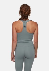 Canotta atletica grigia con design a schiena rotonda e dettaglio del logo. Il tessuto appare liscio con una silhouette aderente.