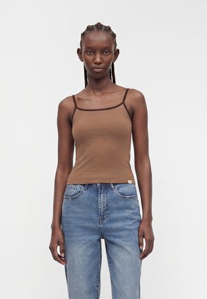 Mannequin femme aux cheveux tressés portant un débardeur marron à fines bretelles et un jean taille haute bleu sur un fond uni.