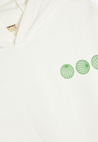 Ljusbeige hoodie med tre gröna globdesigns på framsidan. Tyget har en jämn struktur, med en justerbar huva och en synlig lapp.