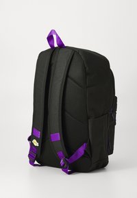 Mochila preta com costas almofadadas, alças roxas, puxadores de zíper roxos e um pequeno logo dos Lakers numa das alças, apresentada sobre um fundo branco.