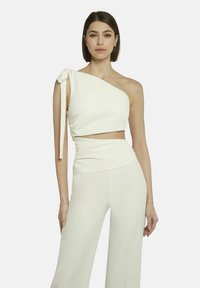 Weißes, einseitiges Crop-Top mit einem Schleifendetail an der Schulter, kombiniert mit hoch taillierten, weit geschnittenen Hosen, beide aus einem glatten, elastischen Stoff.