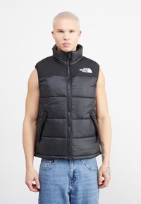 Gilet imbottito nero con collo alto, zip frontale e tasche a toppa. Il gilet presenta un design trapuntato e un logo sul lato sinistro del petto.