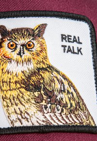 Maroon cap featuring a white patch with an embroidered owl design. Text "REAL TALK" beside the owl, highlighting detailed coloration and texture.