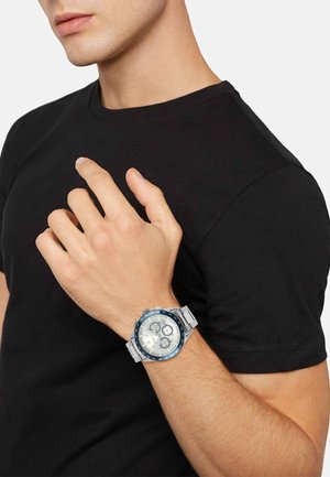 Kronografur med en sølvmetalrem, blå bezel og cremefarvet urtavle, der har tre sub-tavler og selvlysende markeringer.