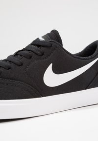 Mustamantel sneakers, millel valge Swooshi logo, tasasel paelad, pehmendatud krae ja tekstuuriga pind, valge kummitald.