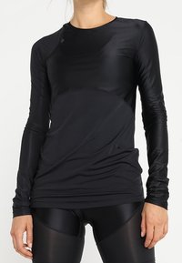 Schwarzes Performance-Oberteil mit langen Ärmeln und nahtlosem Design, mit glatter Textur und figurbetonter Passform. Akzente setzen dezente Nähte.