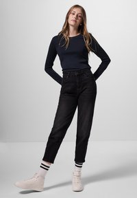 Zwarte high-waisted jeans, strak in de taille, losjes door de benen. Gecombineerd met een marineblauwe longsleeve en witte sneakers met zwarte accenten.