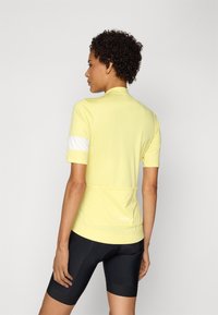 Kortärmad cykeltröja i ljusgul tyg med vita detaljer, en åtsittande design och en bakficka. Kombinerad med svarta cykelshorts.