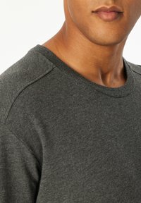 Male wearing a dark gray crew neck sweater, shown from neck to shoulder against a plain white background.