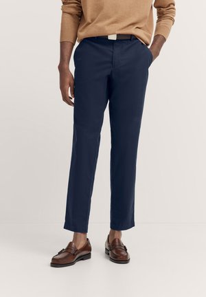 Navyblaue Hose mit einer taillierten Passform, die eine glatte Textur, Seitentaschen und einen klassischen Bund aufweist, kombiniert mit braunen Slippern.