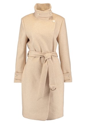 Beige villakangastakki lovettujen kaulusten kanssa, yhdistetty mustavalkoiseen kuvioituun mekkoon ja mustiin slip-on-tennareihin. Sileä pinta ja moderni istuvuus.