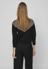 Maglione nero con un design a V marrone sulla schiena. Maniche lunghe, polsini a costine, abbinato a pantaloni neri. Texture complessiva liscia.