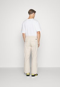 Beige cargo bukser med en afslappet pasform, elastisk talje, to baglommer, båret med en hvid t-shirt og sorte sneakers med gule accenter.