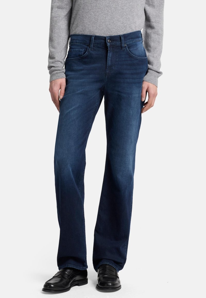 Jeans in denim blu scuro con un taglio dritto, cinque tasche, leggera scoloritura e una chiusura classica con bottone e zip. Indossati con un maglione grigio.