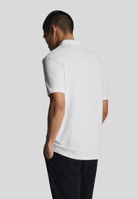 Polo bianco con maniche corte, texture a coste e colletto classico. Vista posteriore, progettato in modo armonioso, abbinato a pantaloni scuri.