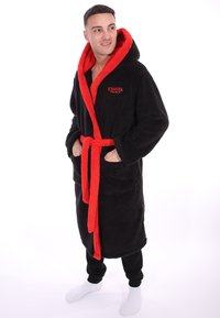 Zwarte fleec bathrobe met een rode pluche kraag en strik, voorzien van zakken. "Stranger Things" logo in het rood aan de linkerkant van de borst. Zachte textuur.
