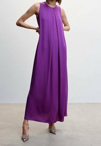Robe maxi violette sans manches avec une silhouette fluide, un tissu doux et un détail plissé à l'avant. Associée à des talons argentés à bouts pointus.