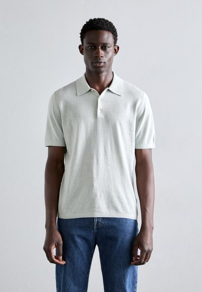 Polo en tissu gris clair, à manches courtes, col avec trois boutons. Associé à un jean en denim bleu pour un look décontracté.