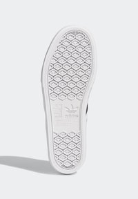 Valkoinen kuminen kengän pohja, jossa on kuusikulmainen kulutuspinta, varustettuna kohokuvioidulla brändäyksellä ja kokotiedoilla kantapäässä ja keskiosassa.