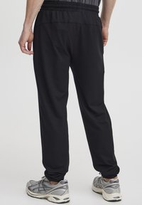 Zwarte sportbroeken met een elastische taille, taps toelopende benen en rekbare stof. Gecombineerd met grijze hardloopschoenen met een gevoerd ontwerp.
