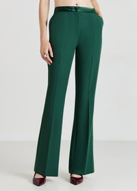Pantaloni larghi verdi e fluido con una cintura in satin liscia, dotati di chiusura frontale con zip e tasche laterali. Colore uniforme, senza fantasie.