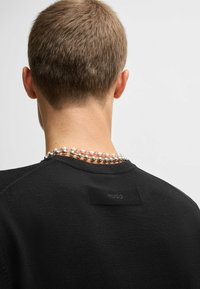Felpa nera con collo rotondo, caratterizzata da un tessuto strutturato e un'etichetta con la scritta "HUGO" sul retro. Accompagnata da una collana di perline.