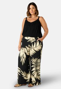 Top nero senza maniche con tessuto texture, abbinato a pantaloni a gamba larga caratterizzati da un motivo di foglie di palma crema su sfondo scuro. Includono sandali.