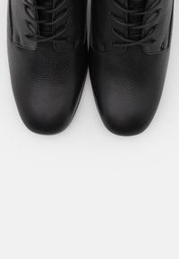 Zapatos de cuero negro con una textura lisa, puntera redondeada y un diseño clásico de cordones; cuentan con costuras destacadas y un detalle mínimo.