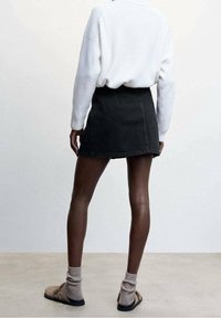 Falda de mezclilla negra con una silueta ajustada, combinada con un suéter blanco texturizado y sandalias beige con calcetines grises. Look suave y casual.