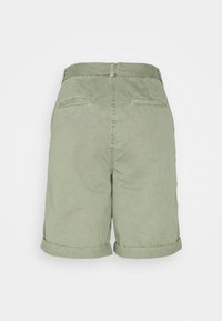 Short vert clair longueur genou avec revers roulés, poches arrière passepoilées, passants de ceinture et couture centrale au dos visible sur fond uni.