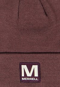 Braune Strickmütze mit umgeschlagenem Bündchen. Verfügt über ein rechteckiges Logopatch mit dem Buchstaben "M" und dem Markennamen "Merrell" in Weiß.
