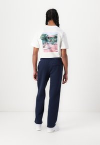 Vit t-shirt med en färgstark landskapstryck på ryggen, kombinerad med marinblå joggers och vita sneakers. Mjukt tyg, avslappnad passform.