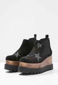 Botas de plataforma de ante negro con acentos de purpurina en forma de estrella, paneles laterales elásticos y una suela de madera en capas con un patrón en zigzag.