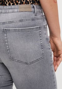 Grå denimjeans med medelhög midja, som har en märkesläderlapp, bakfickor och en slät textur med subtila sömdetaljer.
