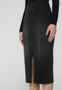 Schwarzer Denim-Rock mit hohem Bund, knielang, mit einem Schlitz auf der Vorderseite und dezenten Nahtdetails. Glatte Textur, taillierte Form.