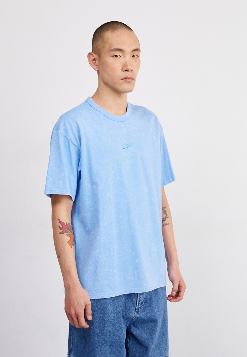 Ανοιχτό μπλε βαμβακερό μπλουζάκι με υφασμάτινη υφή και μικρό, κεντημένο λογότυπο στο στήθος. Κοντά μανίκια και στρογγυλή λαιμόκοψη.