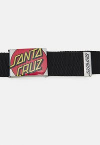 Cinto de tecido preto com uma fivela redonda vermelha e amarela, apresentando "SANTA CRUZ" em letras em negrito. Fecho de metal com detalhe da marca.