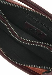 Burgunderfarbene Ledertasche mit einem schwarzen Stofffutter, die zwei Reißverschlussfächer, silberne Beschläge und flache Nähdetails aufweist.