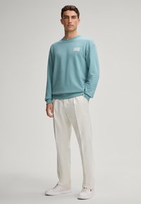 Felpa azzurra chiara con colletto girocollo e patch logo, abbinata a pantaloni bianchi e sneaker bianche. Tessuto morbido con una vestibilità rilassata.