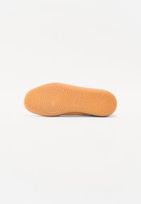 Semelle de chaussure en caoutchouc orange avec un motif de grip circulaire, texturée pour l'adhérence ; comprend un bout lisse et arrondi ainsi que des lignes latérales courbes.