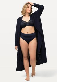 Accappatoio blu navy con maniche lunghe, apertura frontale e texture morbida, indossato sopra un reggiseno in pizzo e una mutandina a vita alta coordinati in blu scuro.