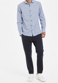 Vaaleansininen nappikauluspaita, jossa on pieni ruutukuvio, pitkähihaiset, yhdistetty tummansinisiin housuihin ja valkoisiin tennareihin.